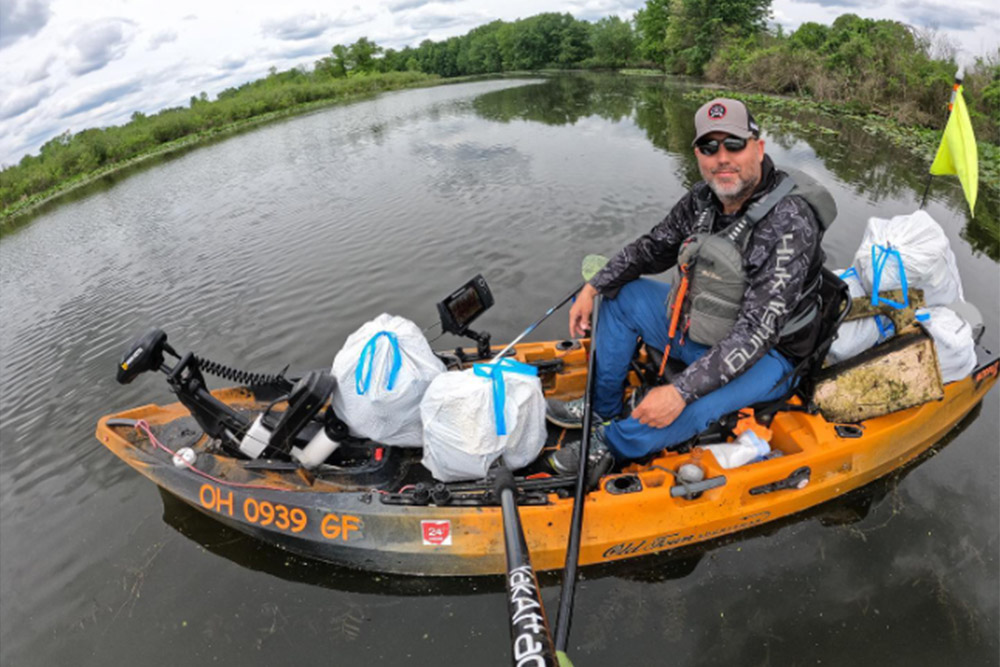 Man in kayak holding several bags of collected trash